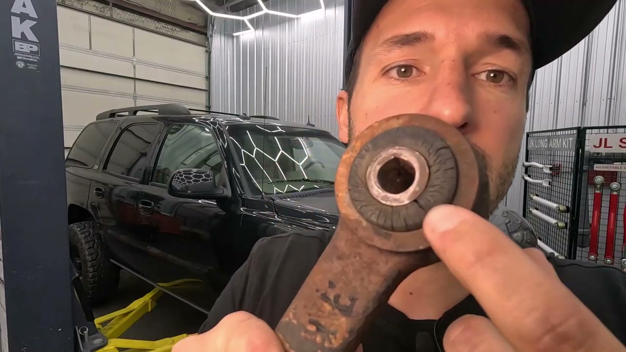 Dry-rotted and cracked factory rubber bushing from a Chevy Tahoe rear control arm held up to the camera